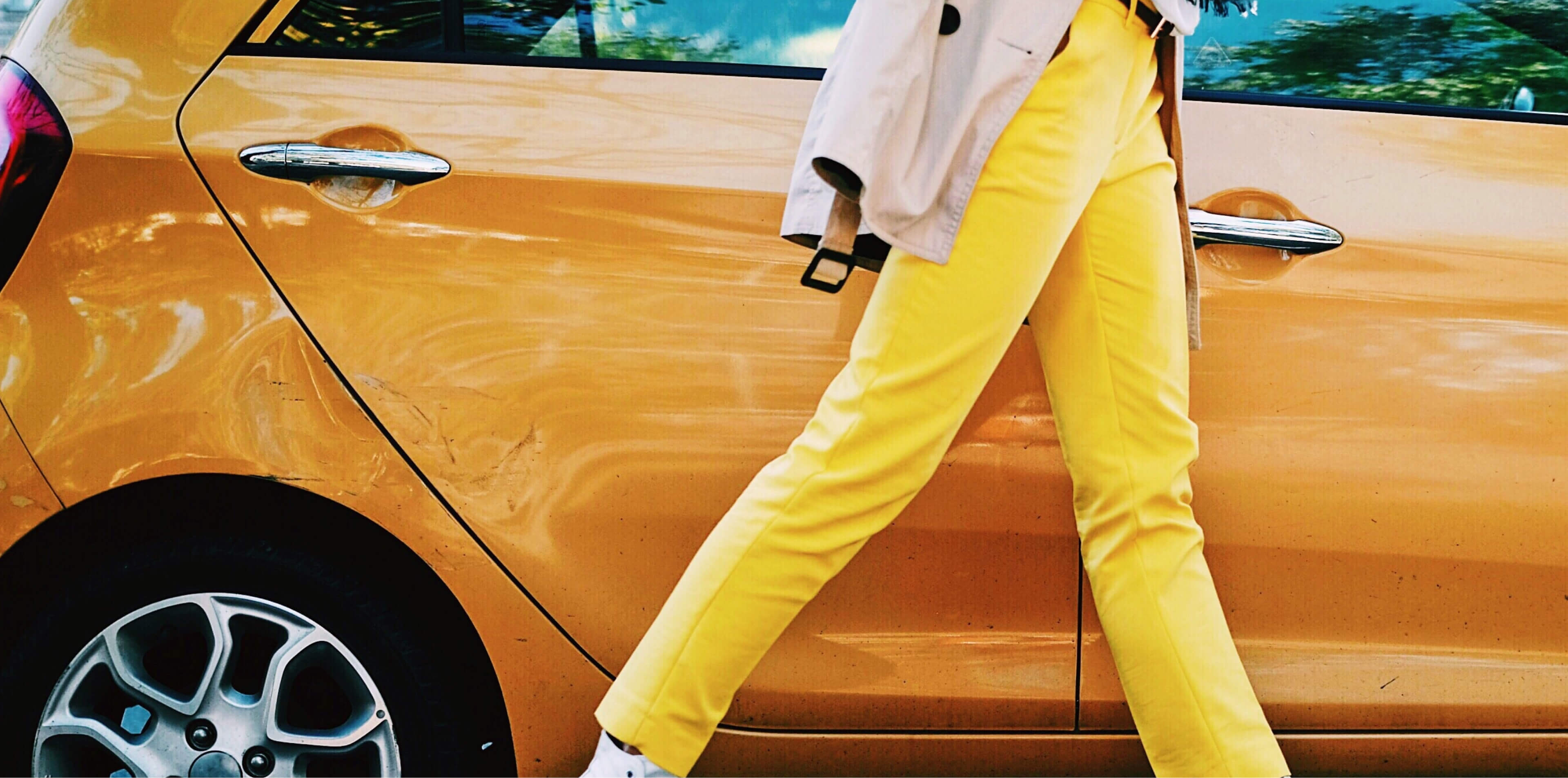 Quirky guy walking briskly beside a yellow car wearing equally bright yellow pants